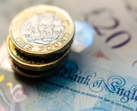 A stack of one pound coins sitting on five and twenty pound notes.